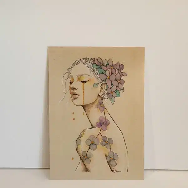 Une impression format carte postale du portrait d'une jeune femme de trois quart, les yeux clos. Elle pleure des larmes d'or. Ses cheveux retenus en chignon sont décorées de fleurs.