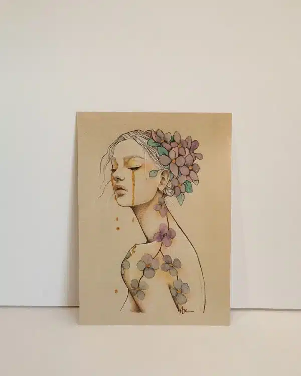 Une impression format carte postale du portrait d'une jeune femme de trois quart, les yeux clos. Elle pleure des larmes d'or. Ses cheveux retenus en chignon sont décorées de fleurs.