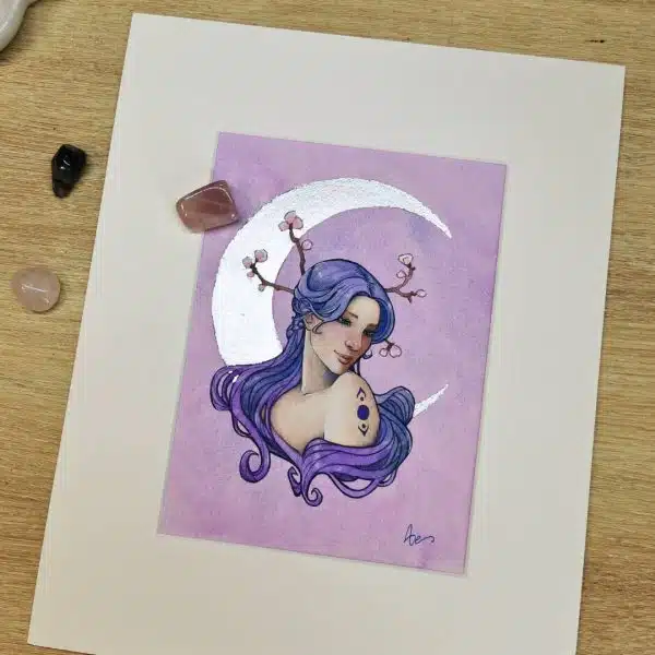 Le portrait d'une jeune femme aux cheveux bleus devant un croissant de lune argenté. L'aquarelle est sertie dans un passepartout en carton blanc. Dans la lune - aquarelle féerique par Aemarielle.