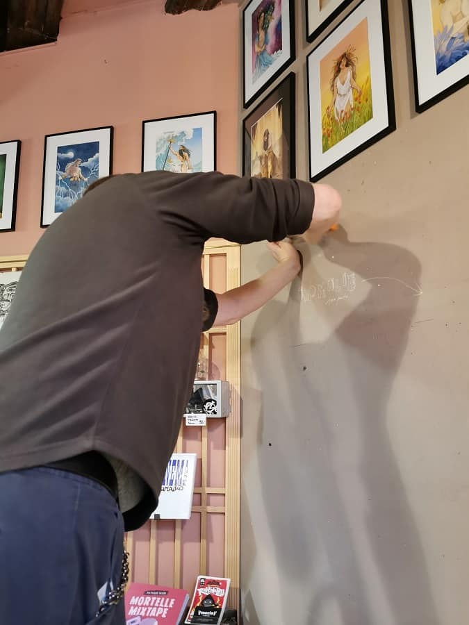Steph en train d'accrocher des aquarelles sur le mur de la librairie.