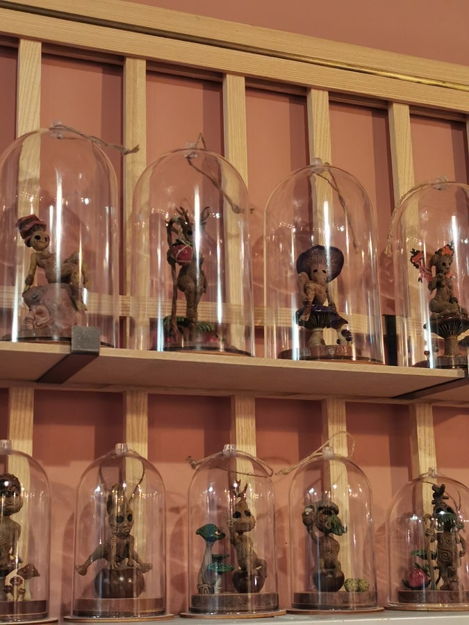 Des figurines en résine de kodama sous cloche sur une étagère de la librairie.