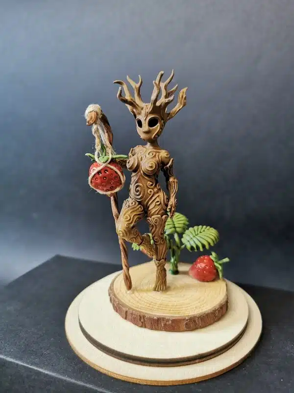 Un kodama féminin debout à côté d'un fraisier, sur un socle en bois.