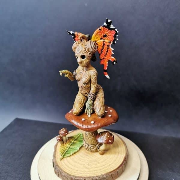 Figurine de kodama féminin aux ailes de papillon sur un socle en bois.