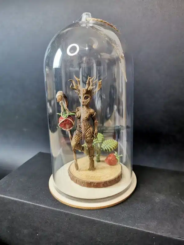 Un kodama féminin debout sous une cloche transparente, tenant un bâton avec une fraise.