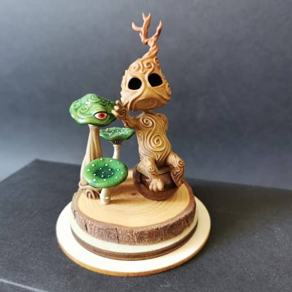 Un kodama en méditation à côté de champignons verts, sur un socle en bois.