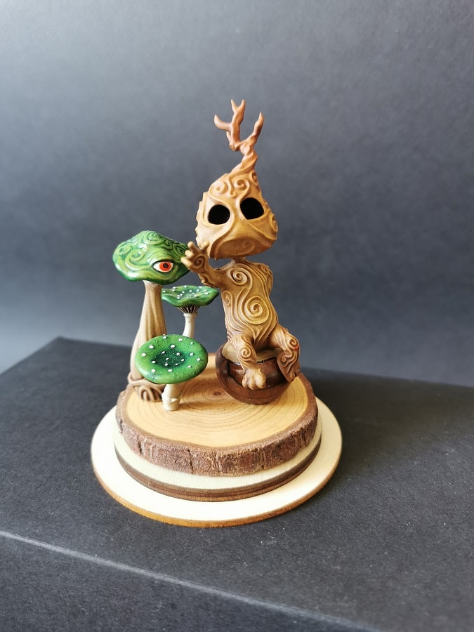 Un kodama en méditation à côté de champignons verts, sur un socle en bois.