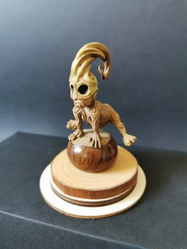 Un kodama en résine sur socle en bois, en train de sauter par dessus un marron.