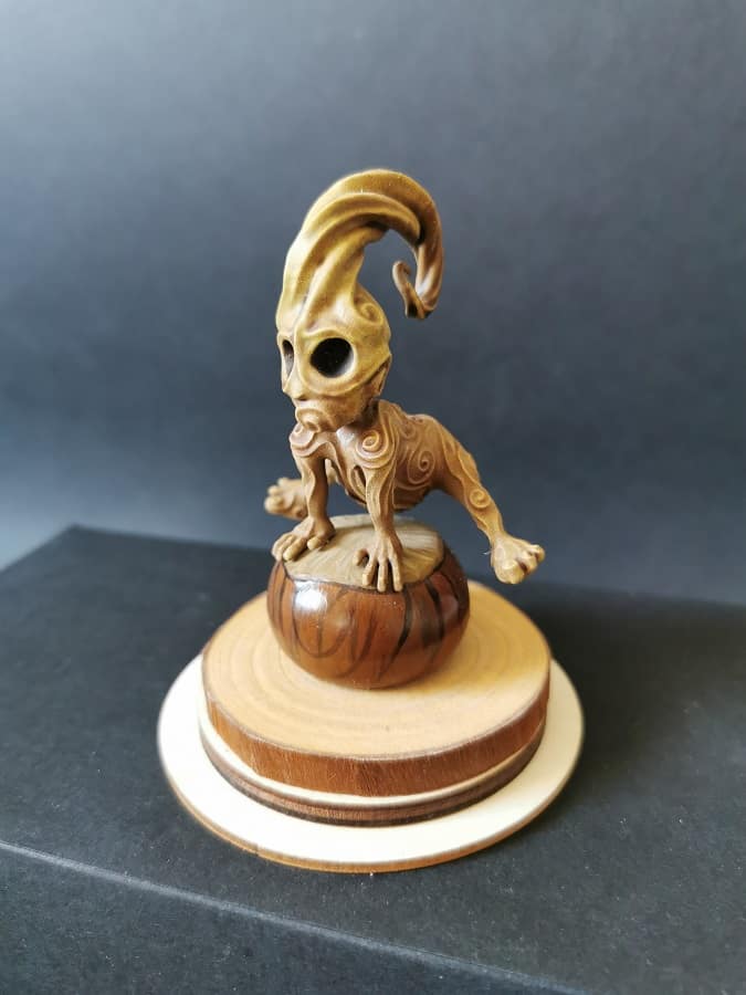 Un kodama en résine sur socle en bois, en train de sauter par dessus un marron.