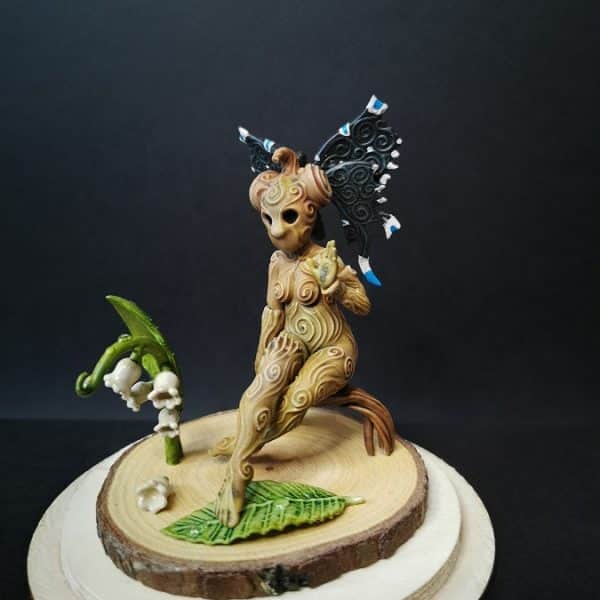 Un kodama féminin sur un socle en bois, dotée d'une coiffe d'ailes de papillon noires