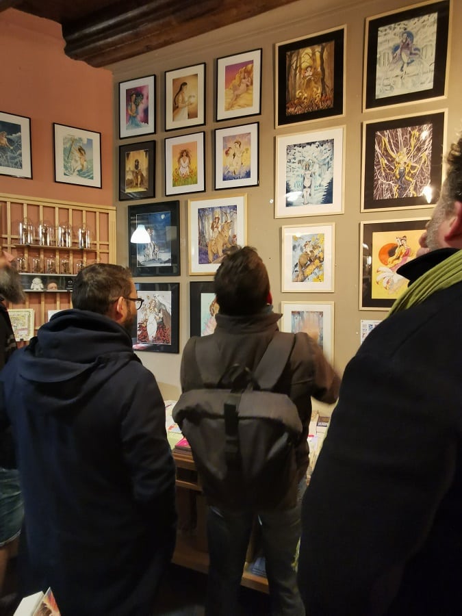 Des visiteurs de l'exposition d'aquarelles orignales, de dos en train d'observer les peintures.