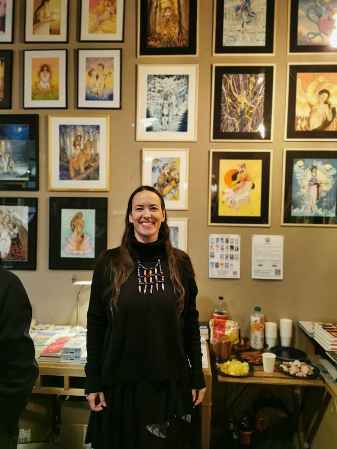 Marie-Gaëlle Aubry, aquarelliste sous le nom d'Aemarielle, debout devant ses peintures exposées sur le mur de la libraire Le Tigre à Strasbourg.