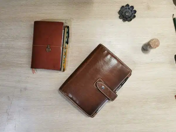 Un classeur Filofax en cuir brun à côté d'un carnet plus petit dans un cuir tirant sur le rouge