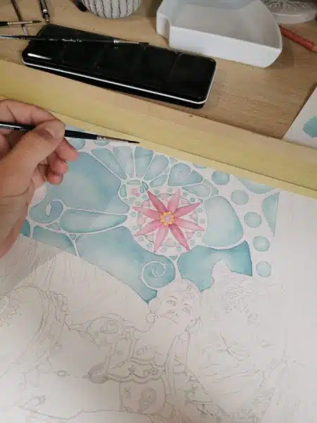 Ma main tenant un pinceau au dessus de l'aquarelle Ganikâ, une courtisane de l'Inde ancienne, alanguie contre un tigre. Seule une partie du décor est peinte en rose et turquoise. L'arrière plan a un côté at nouveau assez marqué.